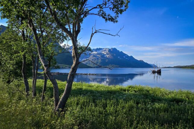Stunning hillsides and trees framing a bright blue lake with old ship floating in it