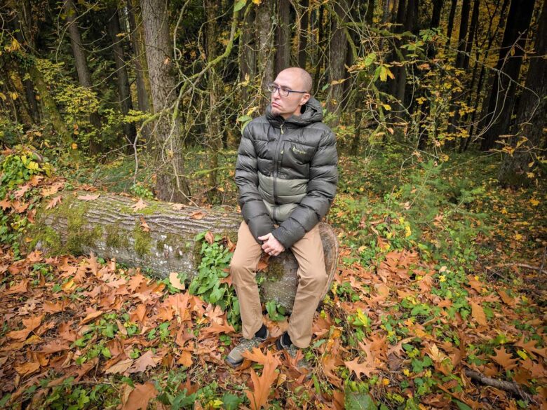 Man wearing Cotopaxi Fuego Max down jacket sitting on log in woods