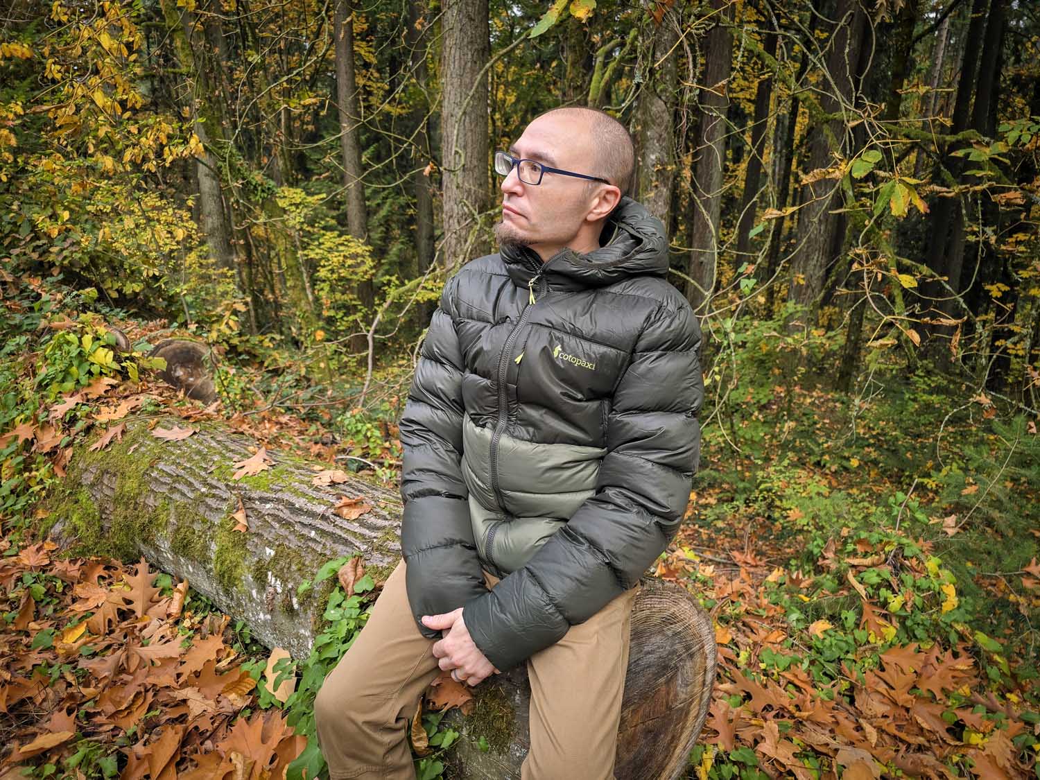 man wearing Cotopaxi Fuego Max down jacket, sitting on large log