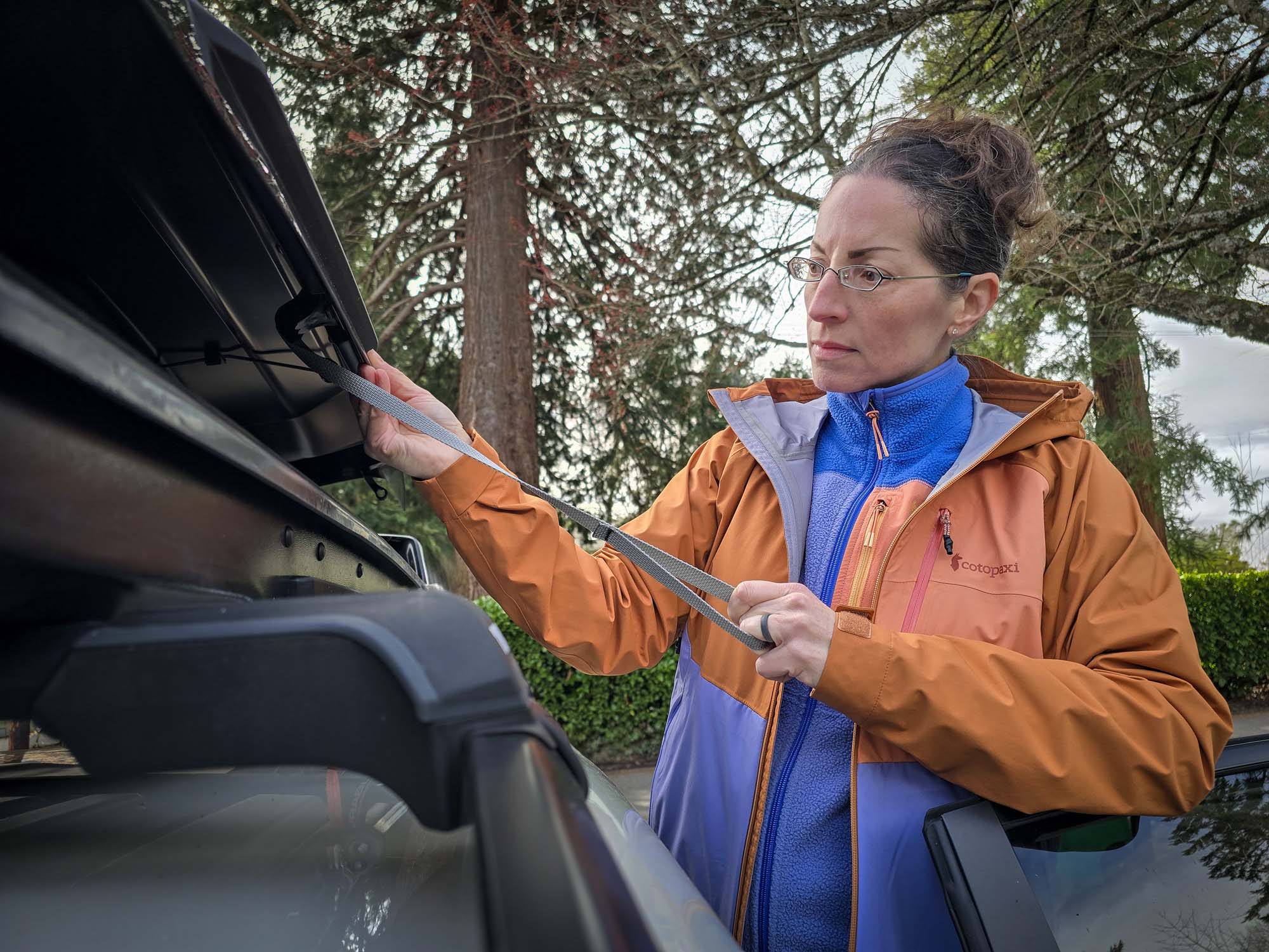 Abrazo Fleece Full-Zip Jacket and Impermeo rain jacket worn by woman closing roof box on car.