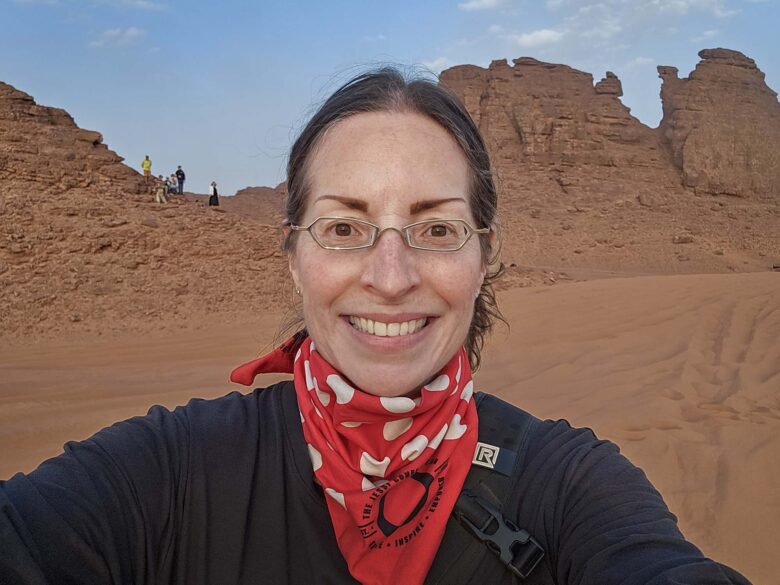 Woman smiling with desert background, wearing a black shirt and red bandana