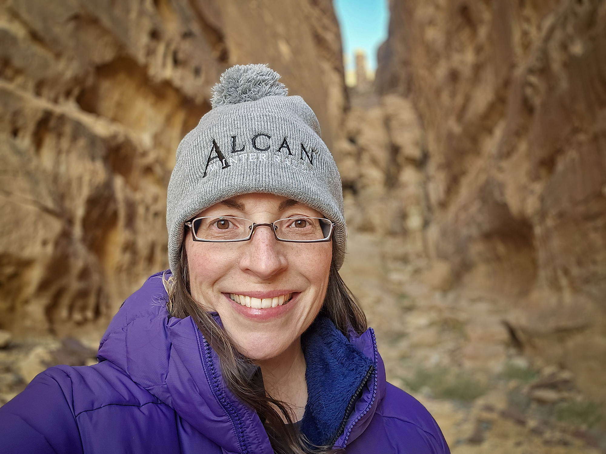 Woman in purple jacket standing in front of rock walls in Saudi Arabia